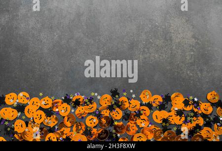 Halloween background: confetti in the shape of orange pumpkins with funny faces, black spiders and stars. Gray background. Copy space. Stock Photo