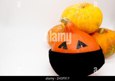 Halloween and covid-19 : Orange pumpkins, one with eyes in a black mask stands on top of the others. Boo. Stock Photo