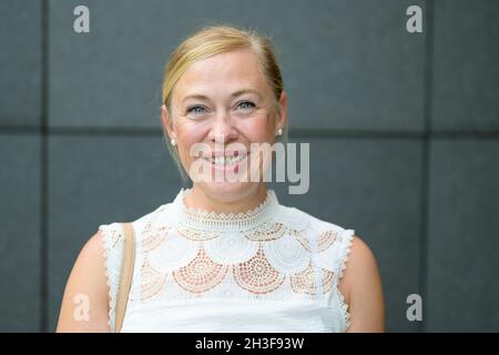 Happy blond woman with smiling blue eyes dressed in a stylish white lacy top smiling happy to the camera Stock Photo