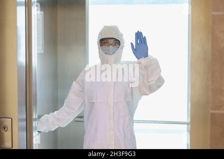 Doctor in protective antiplague suit and glasses waving his hand in corridor of clinic Stock Photo