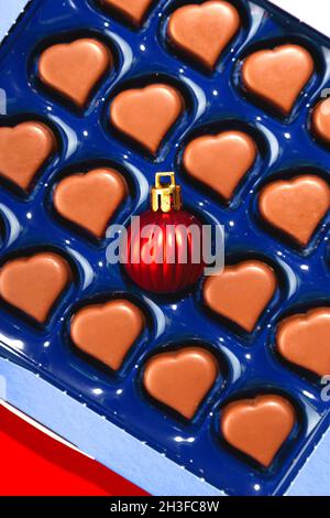 Creative Christmas concept with Christmas ball in box of heart shaped chocolates. Top view. Stock Photo