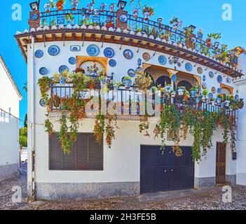 The ornate house, decorated in traditional Andalusian style with ceramic plates, covered with fine blue patterns, green plants and flowers in pots, Al Stock Photo