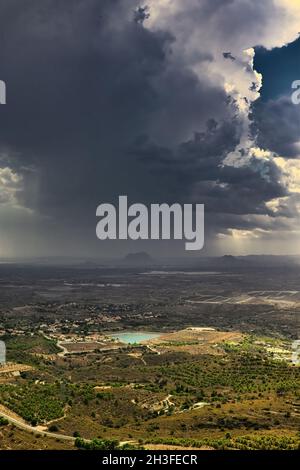 Heavy dark storm clouds gather over a mountain valley near Busot, Spain, Alicante province. Vertical view from top. Stock Photo