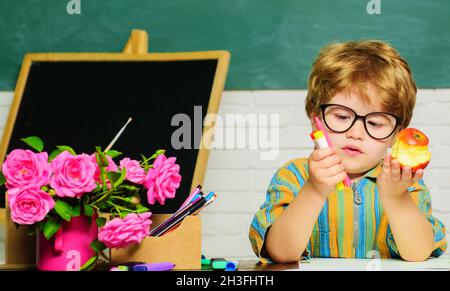 School lunch. Schoolboy in classroom eating apple. Healthy food for kids. Elementary school kid sitting at desk. Stock Photo