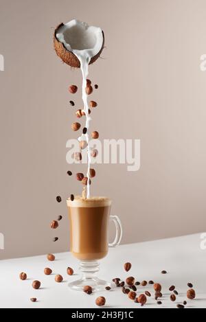 Glass cup with cappuccino and fragrant foam, coconut milk, hazelnuts, planted coffee beans. Coffee concept with vegetarian milk. Cup with cappuccino, Stock Photo