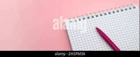 A blank checkered sheet of paper. Notepad and pen on pink. Pink Pen. Notepad spring Spiral spiral checked sheets. Stock Photo