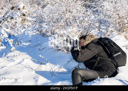photographer shoots icy snowy low trees on a sunny winter day in deep snow. Photographer with a photo backpack Stock Photo