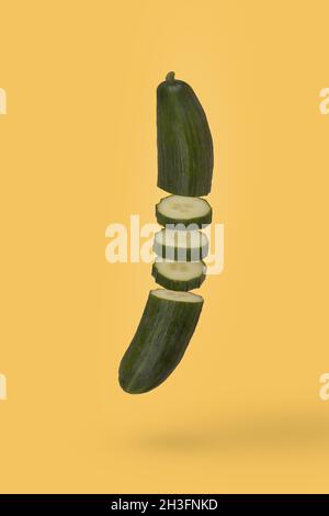 Minimal idea with fresh sliced cucumber floating in air isolated on pastel yellow background. Diet, vitamins, vegan and healthy food. Minimal food or Stock Photo