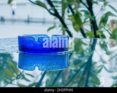 Blues glass ashtray on wet glass table with reflections Stock Photo