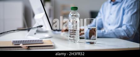 Water Bottle And Drinking Glass On Desk And Man Using Computer Stock Photo