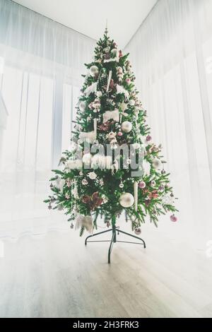 elegant luxurious decorated christmas tree inside the house with white adornments and decorations staying by the window Stock Photo