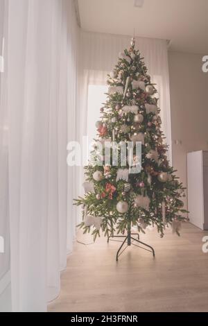 elegant luxurious decorated christmas tree inside the house with white adornments and decorations staying by the window Stock Photo
