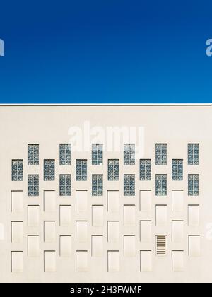 Rectangular windows and niches in the outer building wall against blue sky. Architectural elements repeating pattern of the modern built structure. Stock Photo