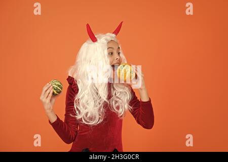 kid wear devil horns having long white hair wig feel hunger and eating halloween pumpkin, happy halloween Stock Photo