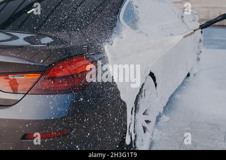 Car exterior cleaning, applying snow foam on dirty auto surface from high-pressure washer Stock Photo