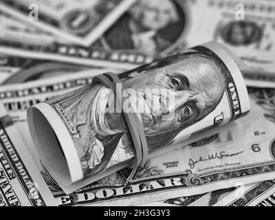 A tied stack of one hundred dollar bills on a dollar bill background. Black and white. Close up