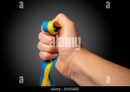 Woman hand holding yellow and blue, Ukrainian national flag colors, fabric ribbon on black background. Ukraine nation independence celebration, patrio Stock Photo