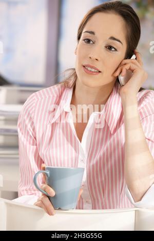 Woman in office having coffee and phone call Stock Photo