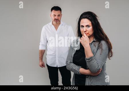 A woman beaten by her husband standing behind her and looking at her aggressively. Domestic violence. Stock Photo