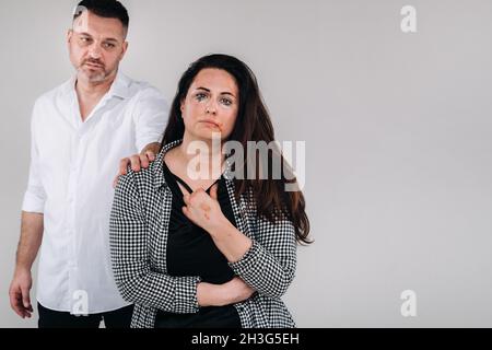 the male rapist put his hand on the shoulder of the beaten woman on a gray background. Domestic violence. Stock Photo