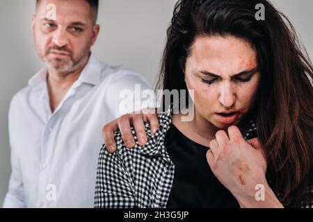 the male rapist put his hand on the shoulder of the beaten woman on a gray background. Domestic violence. Stock Photo