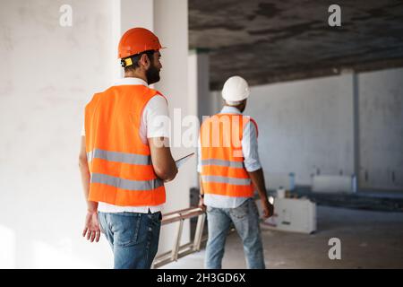 Two young male engineers in uniform and hardhats working at construction site Stock Photo