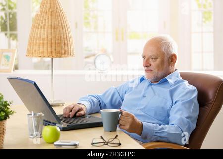 Elderly man using computer, having coffee Stock Photo