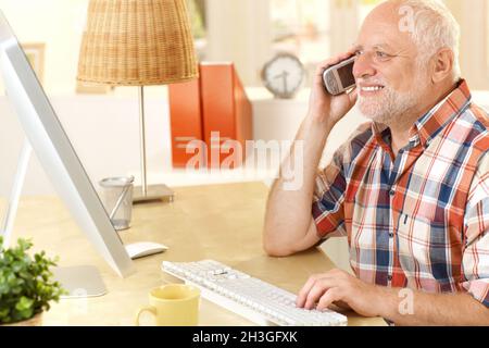 Senior man talking on cellphone, using computer Stock Photo