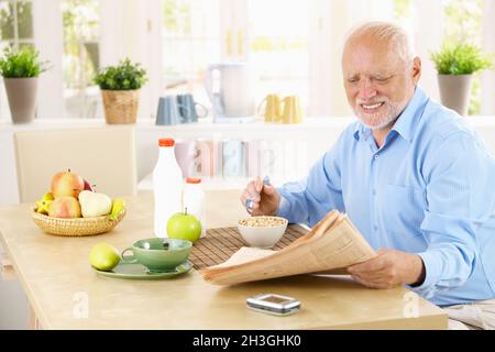 Older man reading newspaper in kitchen Stock Photo