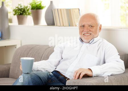 Smiling elderly man having coffee on sofa Stock Photo