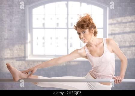 Ballerina girl stretching by bar in studio Stock Photo