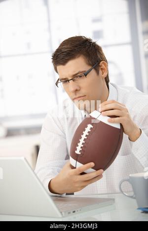 Businessman concentrating on work, holding football Stock Photo