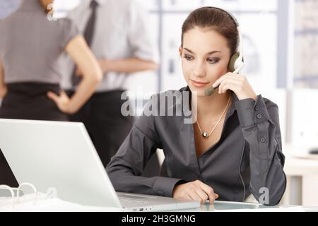 Young office worker using headset sitting at desk Stock Photo