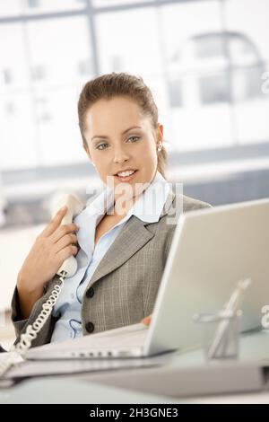 Pretty female using phone and laptop in office Stock Photo