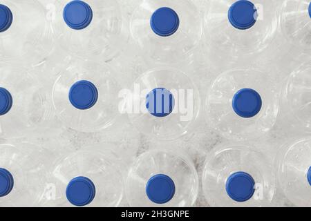 Seen from above, several empty clear plastic water bottles with blue caps standing upright. Stock Photo