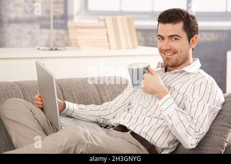 Young man browsing Internet at home smiling Stock Photo