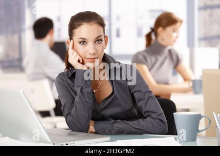 Young woman sitting at desk others working behind Stock Photo