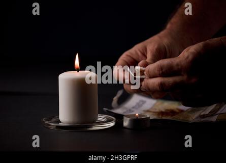 candle lit with flame, man's hands holding a cigar, black background. (focus on candle). Stock Photo