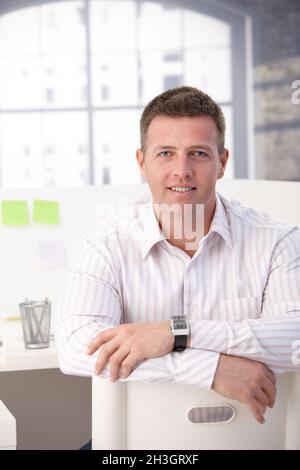 Young male office worker sitting in office smiling Stock Photo