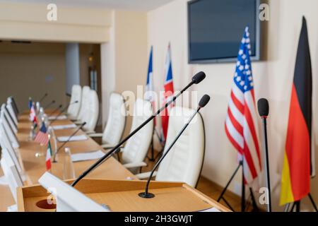 Empty wooden rostrum stand with microphones in conference room with national flags behind long table Stock Photo