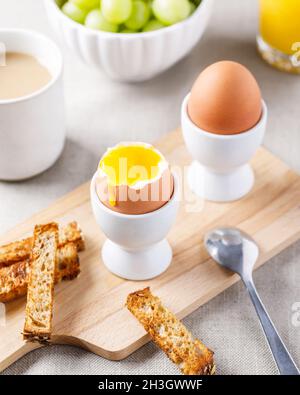 Two soft-boiled eggs in egg cups served on wooden cutting board with toasted bread for breakfast. Food background. Stock Photo