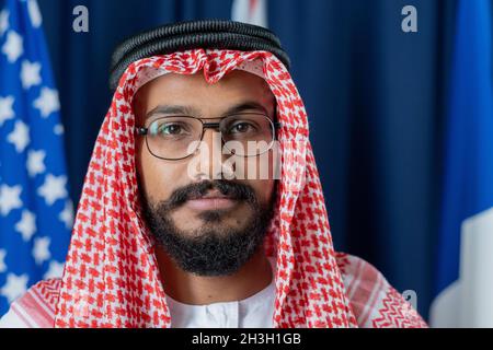 Portrait of serious confident Muslim politician in national dress posing against dark blue curtains and flags Stock Photo