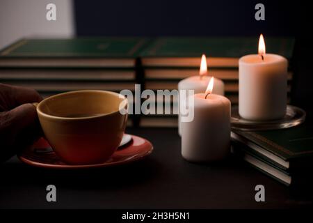 cup of coffee with hot smoke and three burning candles. on the desk at home, power outage (focus on cup). Stock Photo