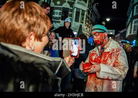 Arnhem, Netherlands. 28th Oct, 2021. A woman is seen taking a photo of a zombie dressed as a doctor. Last two years the zombie walk was canceled due to the Coronavirus pandemic, however this year, the zombies were allowed to stagger through the inner city of Arnhem in search of fresh brains. The walk started at the Live music venue 'Willemeen', where make-up artists were creating their zombie makeups. Also each year, during the parade, the organization collects animal food, to give to an animal shelter, in Arnhem. Credit: SOPA Images Limited/Alamy Live News Stock Photo