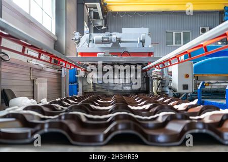 Metal roof tiles made from galvanized steel in metal sheet forming machine in metalwork factory. Stock Photo