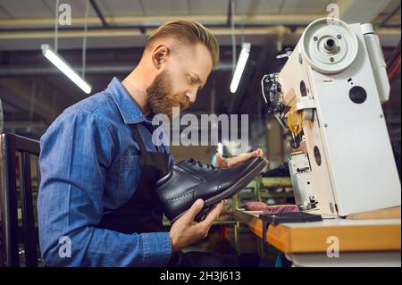 Man shoemaker in uniform holding shoe working at footwear factory workplace Stock Photo