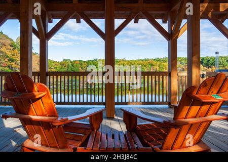 Adirondack chairs on the deck of a covered pedestrian bridge, facing a lake and a forest in fall colors. Enchanta Bridge, Moore State Park, Paxton, MA Stock Photo