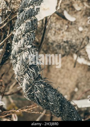 E VERTICAL Close up Macro black old fishing intertwined roughly twisted cotton rope braid detail on sea sand ground. Concept team work, symbol strong Stock Photo