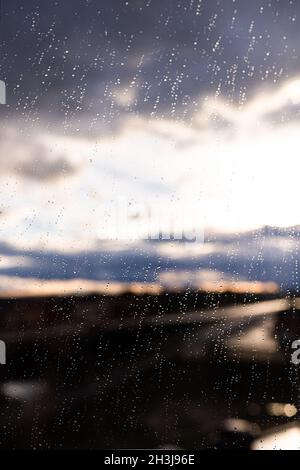 Raindrops on glass or window through which you can see the sky and sunset. Autumn backgrounds and textures. Stock Photo