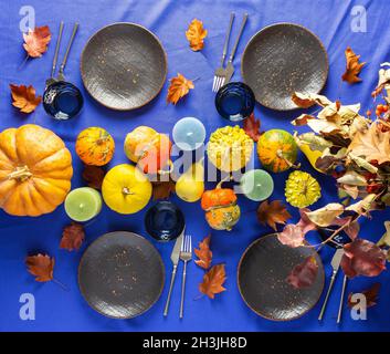 Thanksgiving table setting, bouquet with dry branches, various pumpkins and candles, plates with cutlery and glasses on a blue-purple tablecloth Stock Photo